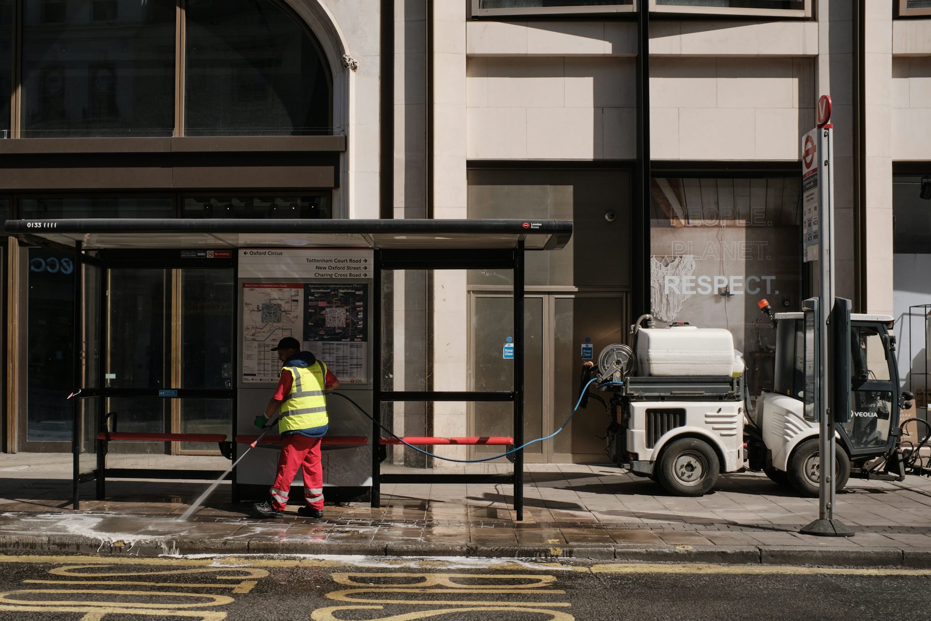 A man in red and hi-vis yellow with street cleaning apparatus on an urban pavement.