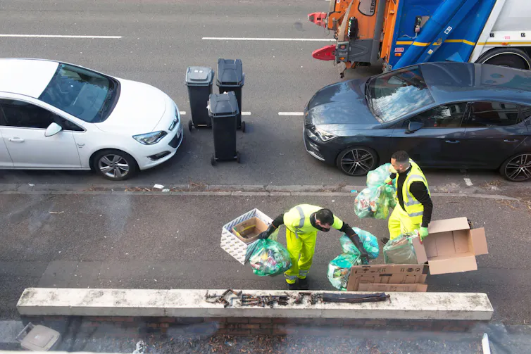Two refuse workers on a street.