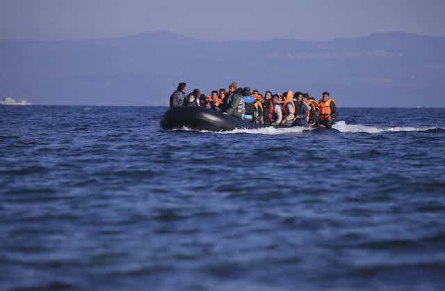 A dinghy full of men in lifejackets on a blue sea in 2015, reaching the Greek island of Lesbos