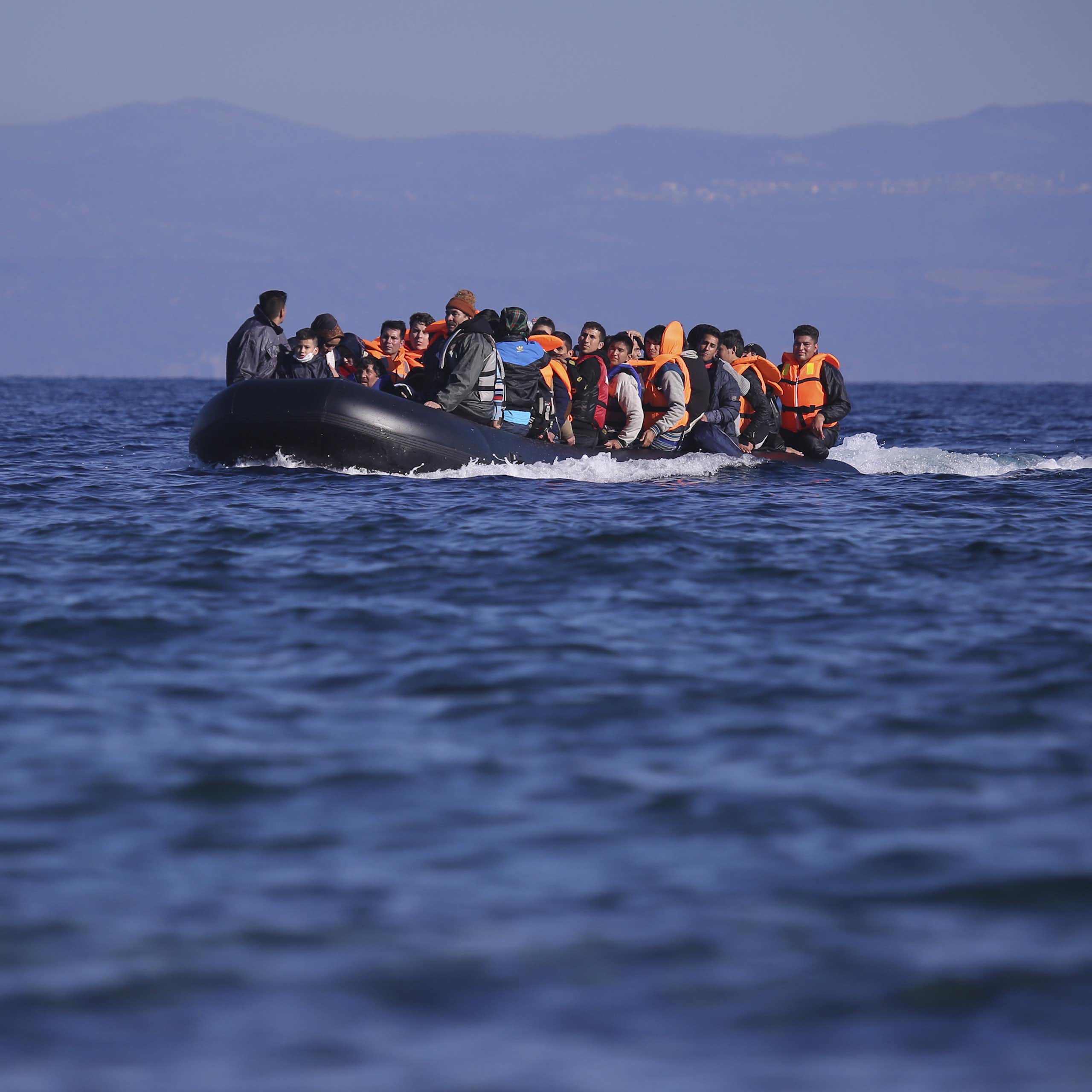 A dinghy full of men in lifejackets on a blue sea in 2015, reaching the Greek island of Lesbos