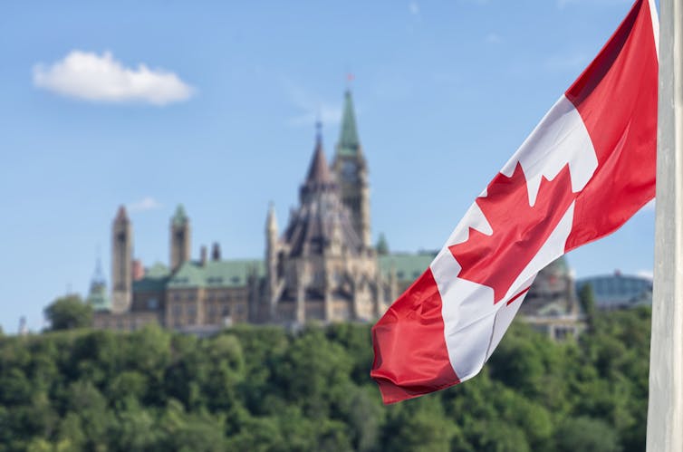 A Canadian flag in the foreground, parliament buildings in the background