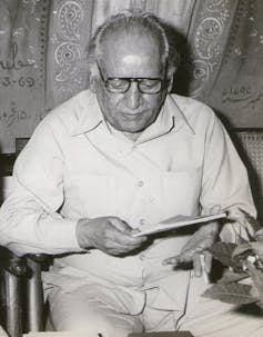 Black and white portrait of a man with glasses sitting and reading.