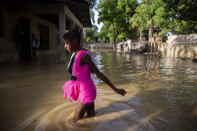 A girl in pink wades through flood waters.