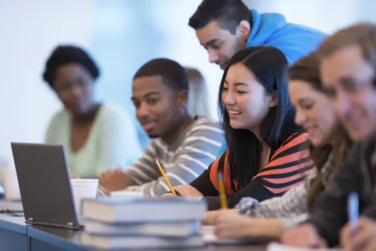 College students look at a laptop sitting on a desk.