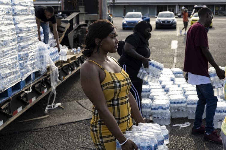 A woman hands out cases of bottled water.