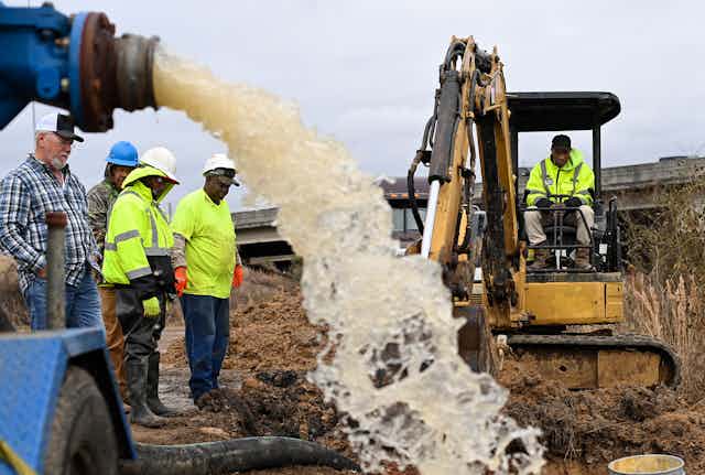 Water gushes from a pipe draining a work area as workers try to figure out how to fix a broken water main.