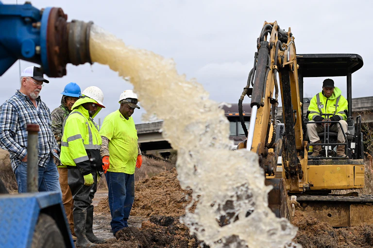 Water gushes from a pipe draining a work area as workers try to figure out how to fix a broken water main.