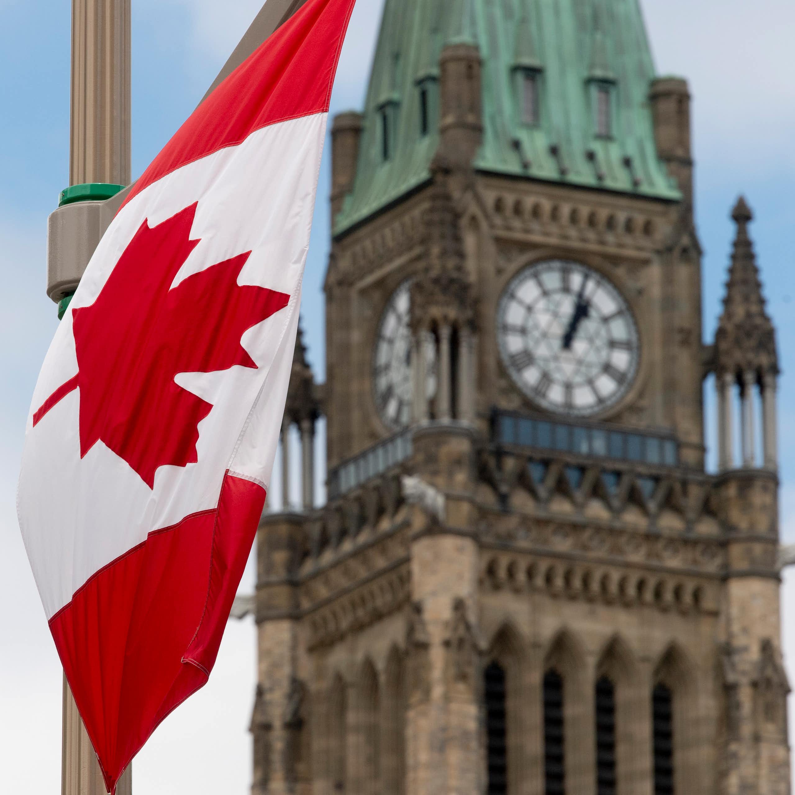 A Canadian flag hands in front of a clock tower