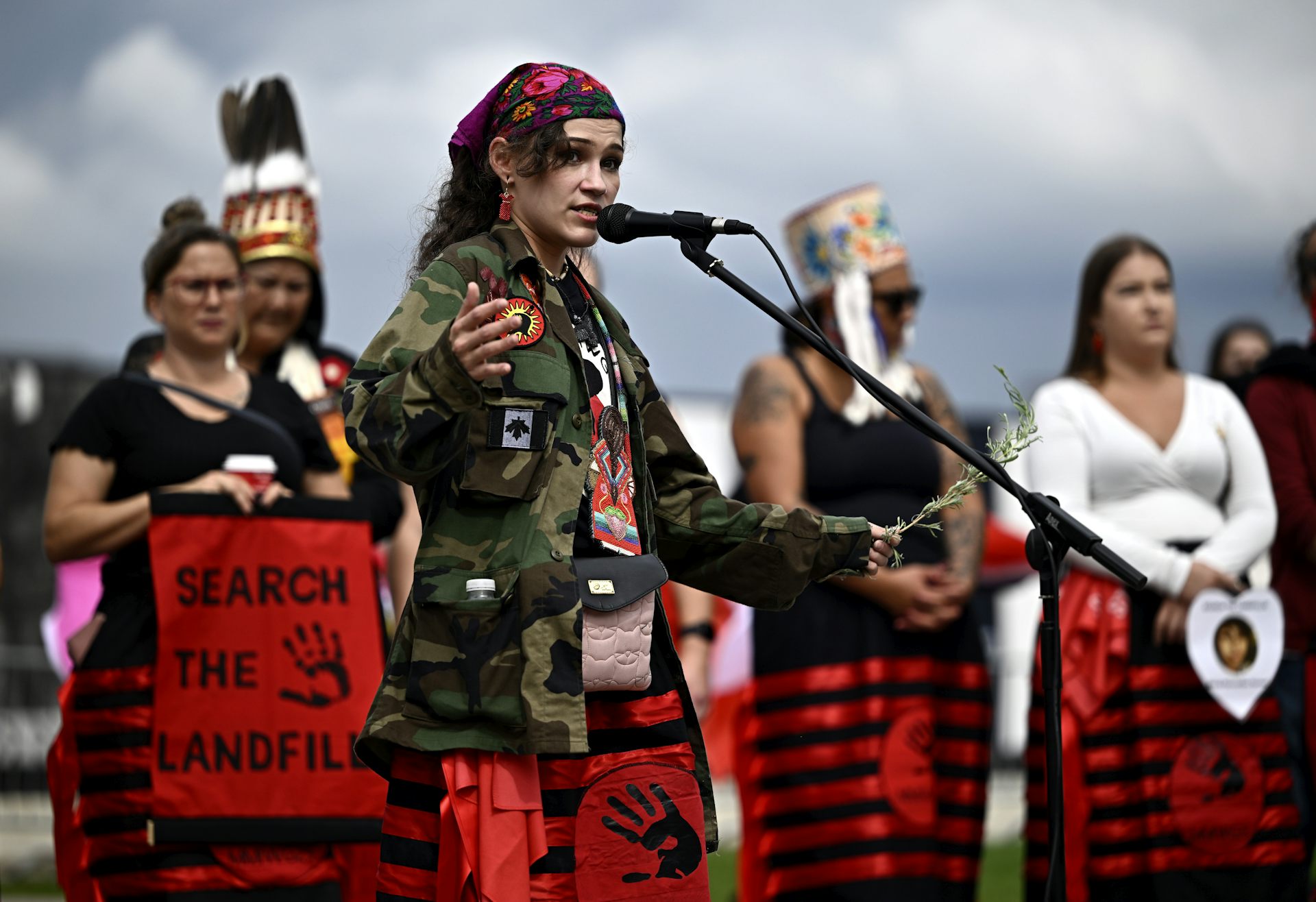 Indigenous women carrying signs that read Search the Landfills speak at a rally.