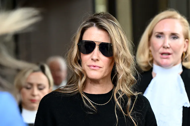 A woman wearing dark aviator glasses leaves a courtroom