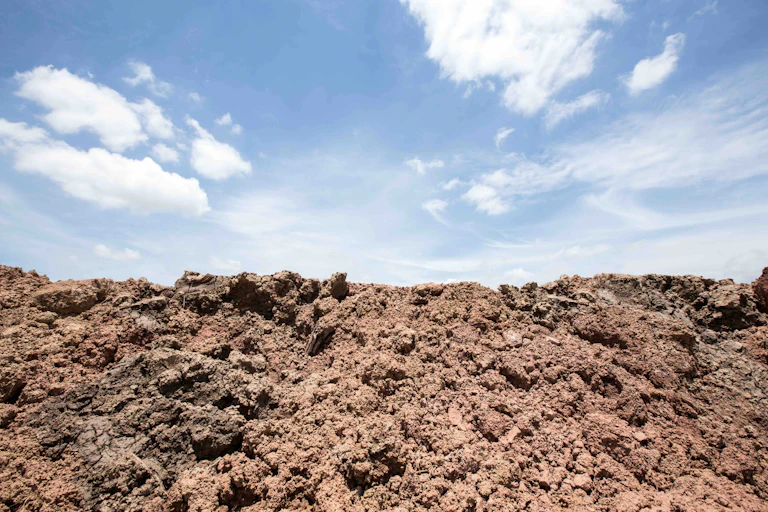 Photo showing disturbed soil beneath a blue sky with some white clouds.