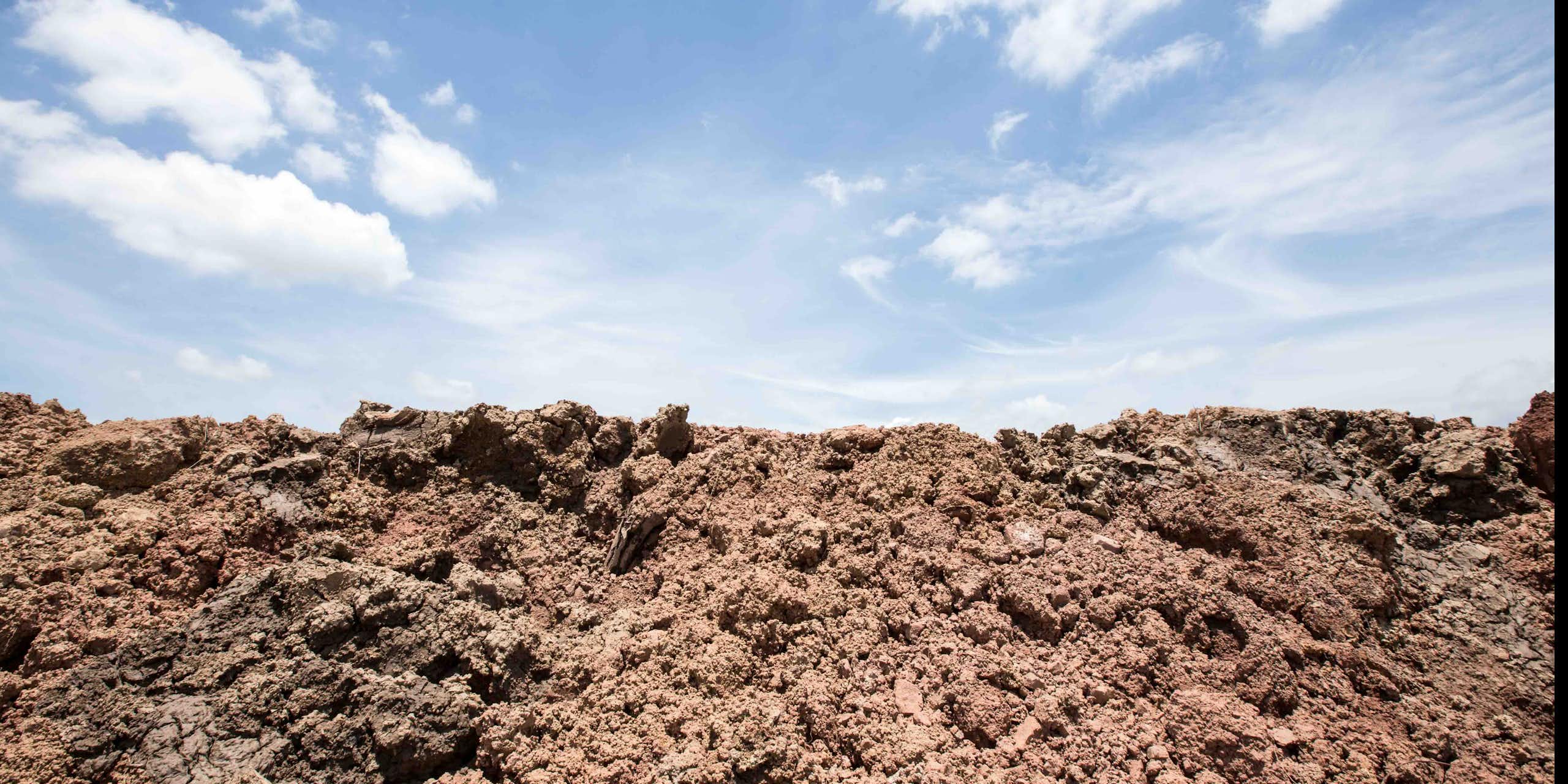 Photo showing disturbed soil beneath a blue sky with some white clouds.