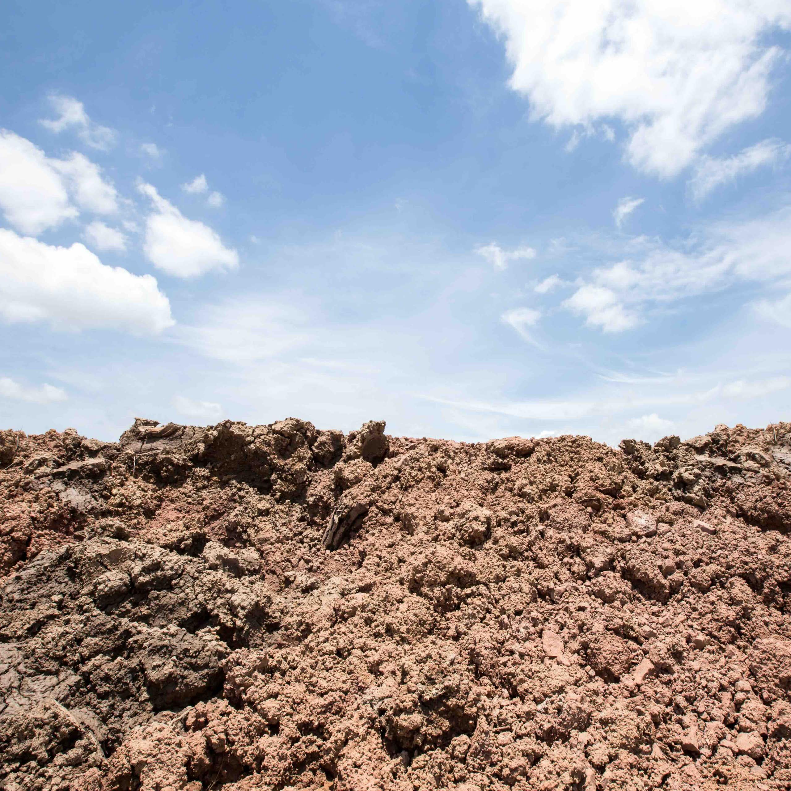 Photo showing disturbed soil beneath a blue sky with some white clouds.