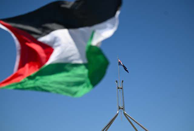 Close-up of Palestinian flag with Australian flag flying from Parliament House in the background