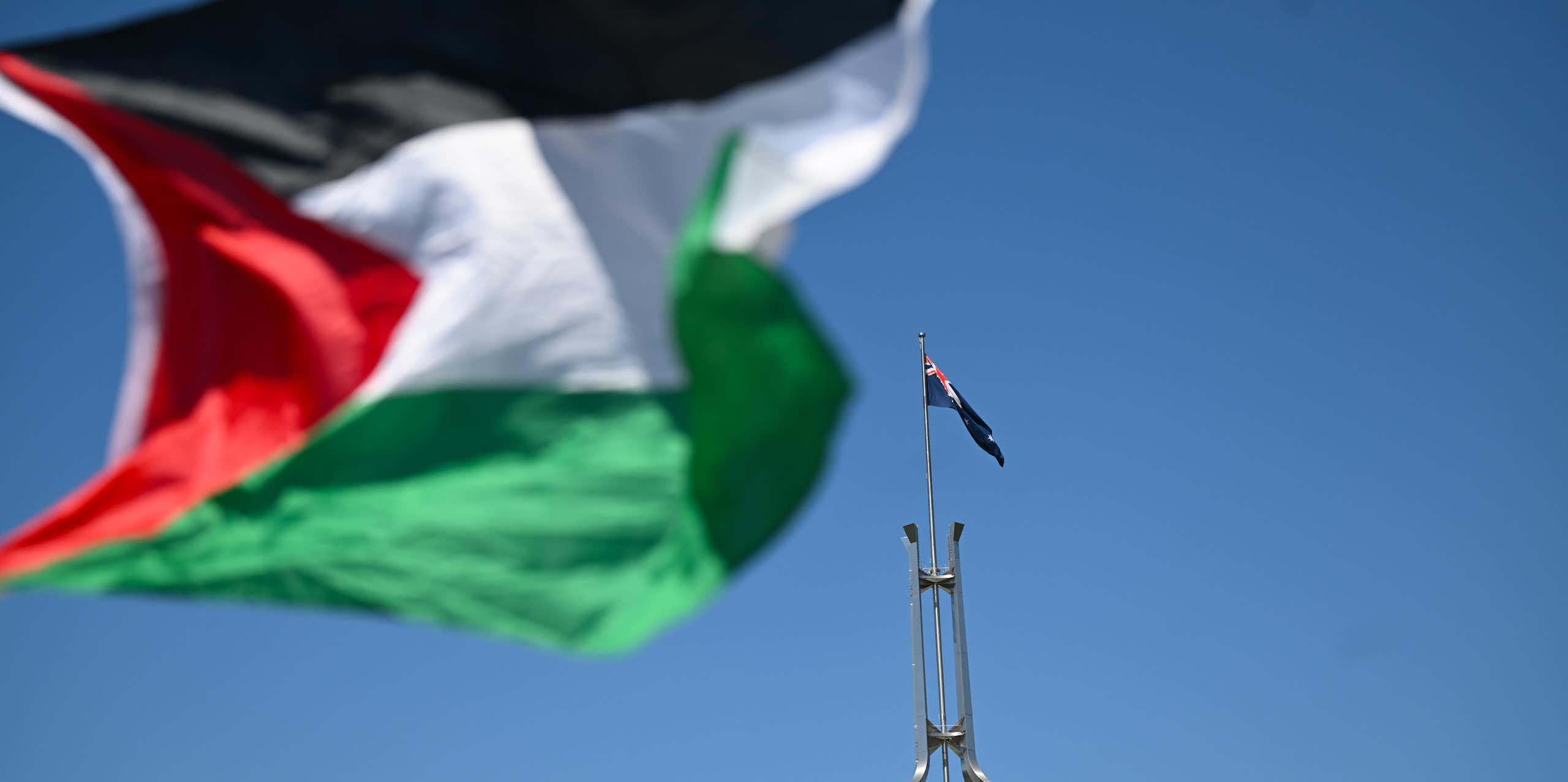 Close-up of Palestinian flag with Australian flag flying from Parliament House in the background