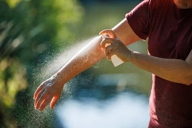 A person sprays insect repellent on their arm.