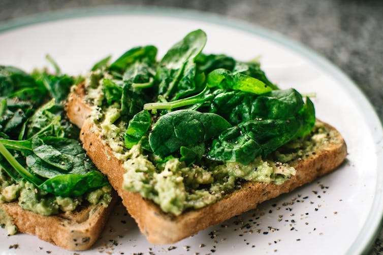Baby spinach and avocado on two slices of toast, on a plate.