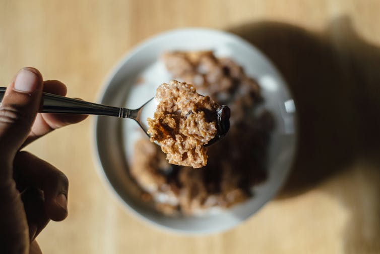 A person holds a spoon of cereal above a bowl of cereal.