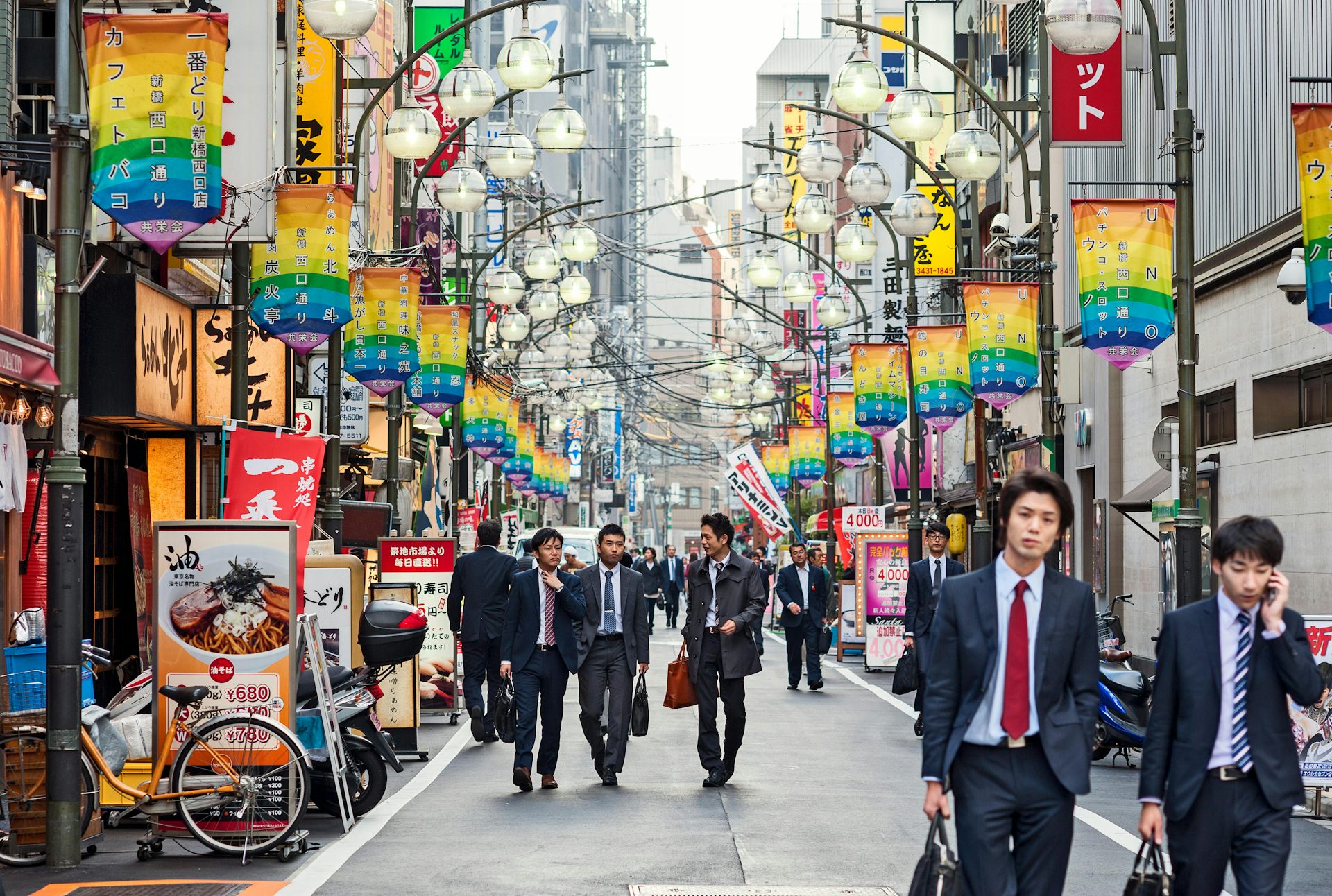 Men dressed in suits walking down a colourful street in Japan.
