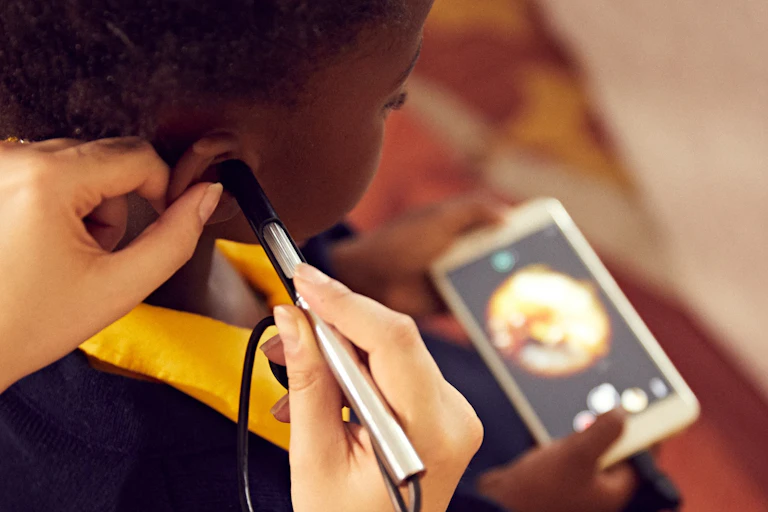 Adult hands hold a device to the ear of a child who is holding a smartphone
