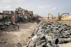 A row of houses right next to a beach and about 3 metres away a wall of rocks piled on top of each other