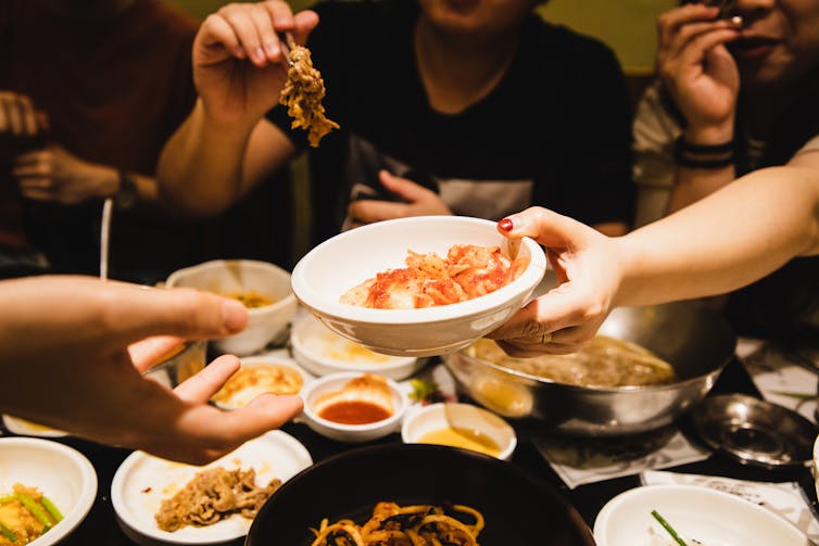 One person passes a dish of kimchi across a table to another person
