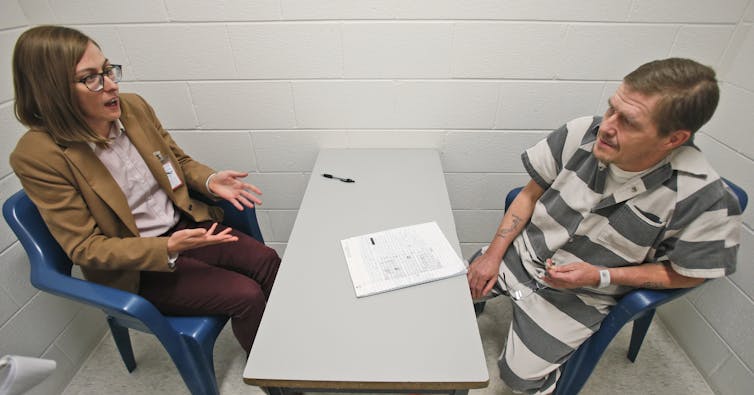 man in striped clothes sits across table from woman in suit jacket