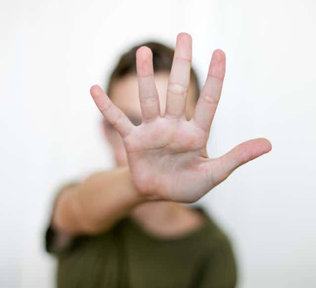 Uma pessoa com um braço esticado, com a palma da mão voltada para a câmera e os dedos estendidos.