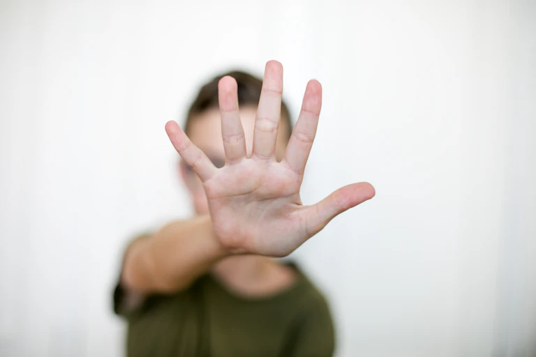 Uma pessoa com um braço esticado, com a palma da mão voltada para a câmera e os dedos estendidos.