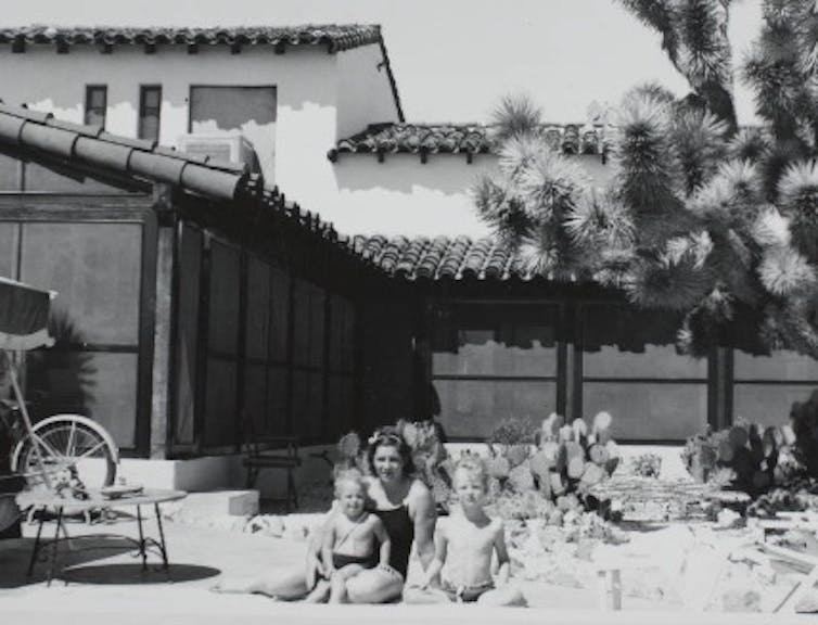 Fotografía en blanco y negro de una mujer en traje de baño y dos niños en traje de baño posando junto a una piscina.