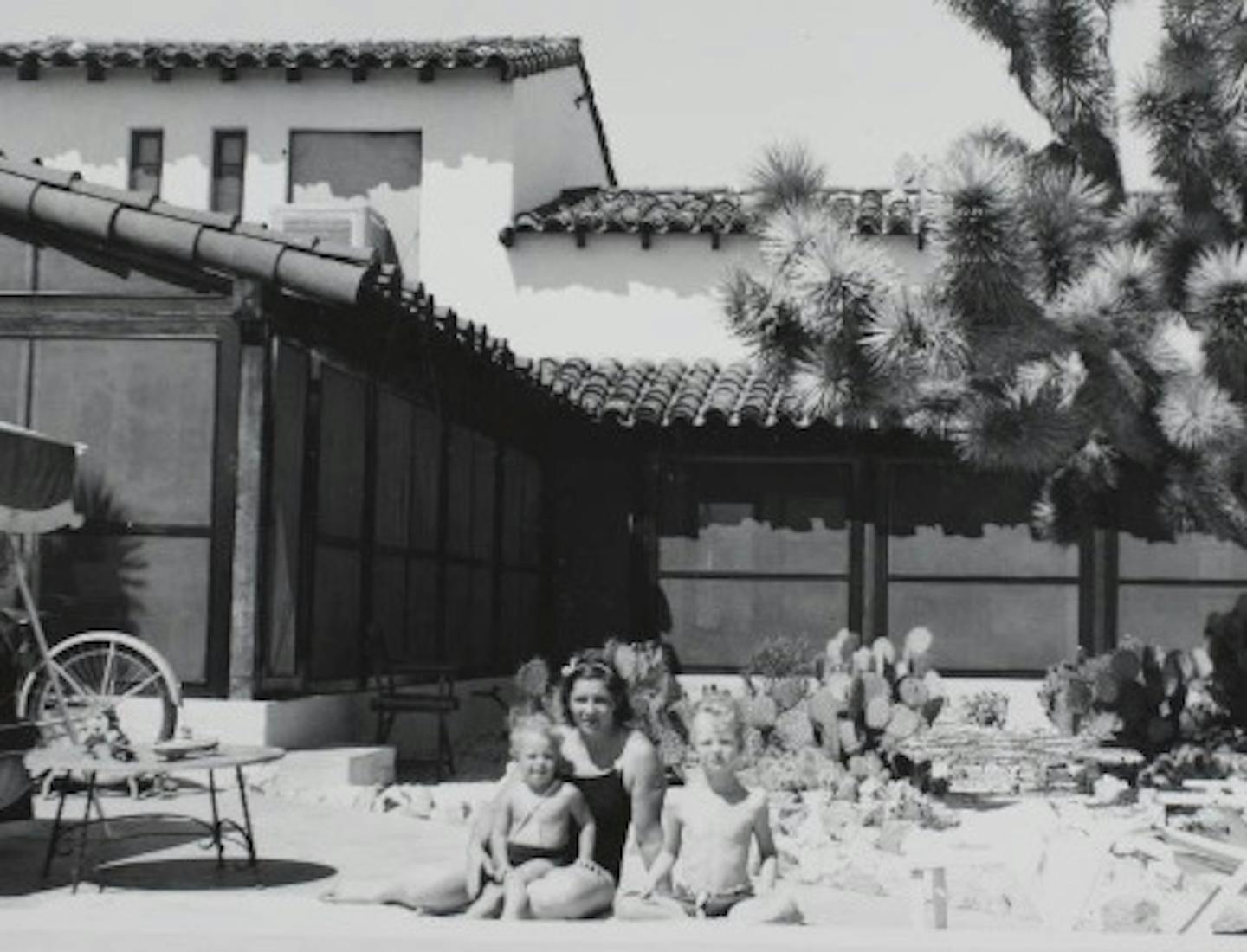 Black and white photo of woman in bathing suit and two boys in bathing suits posing by a swimming pool.