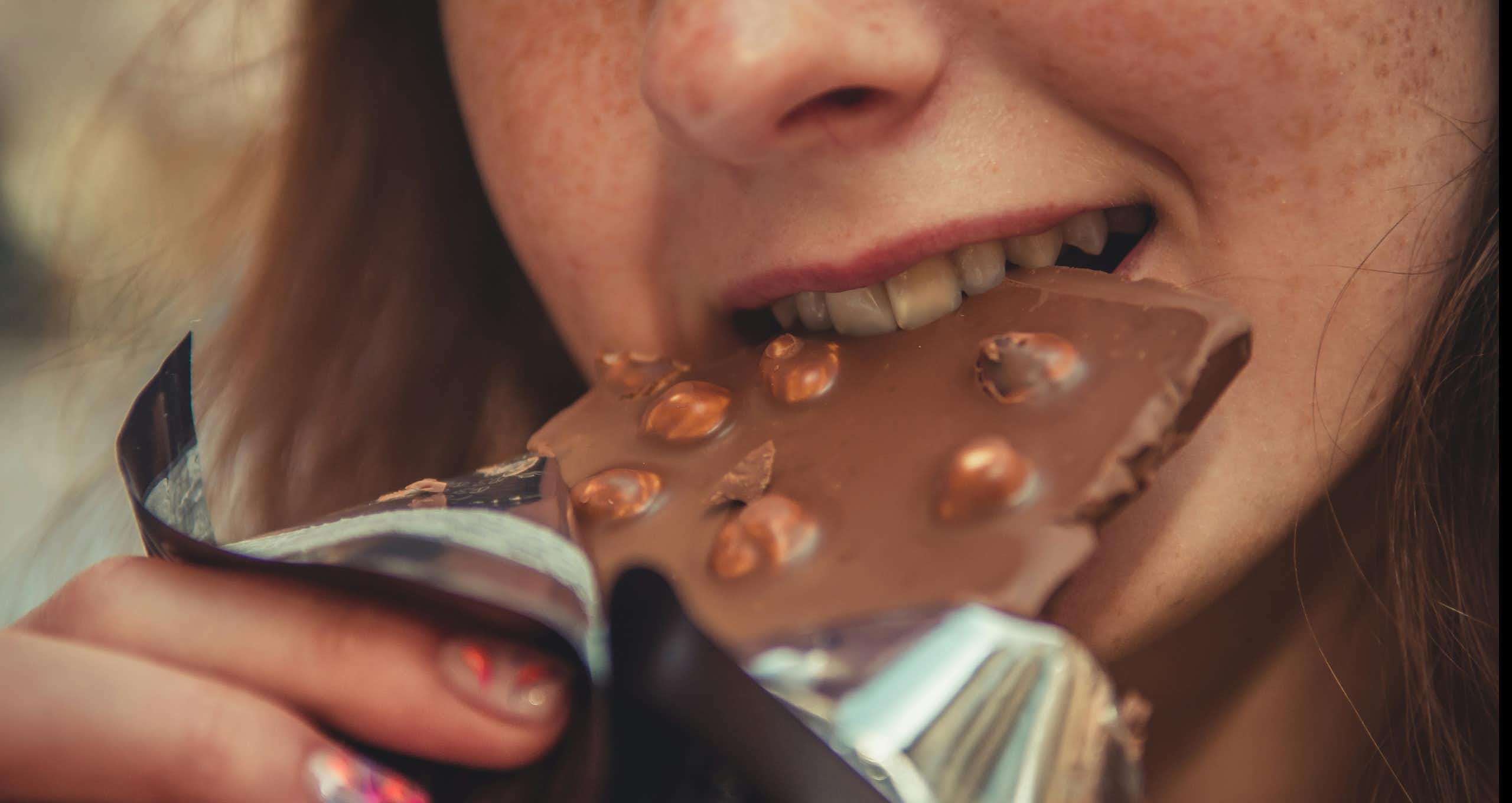 Uma mulher mordendo uma barra de chocolate com avelã