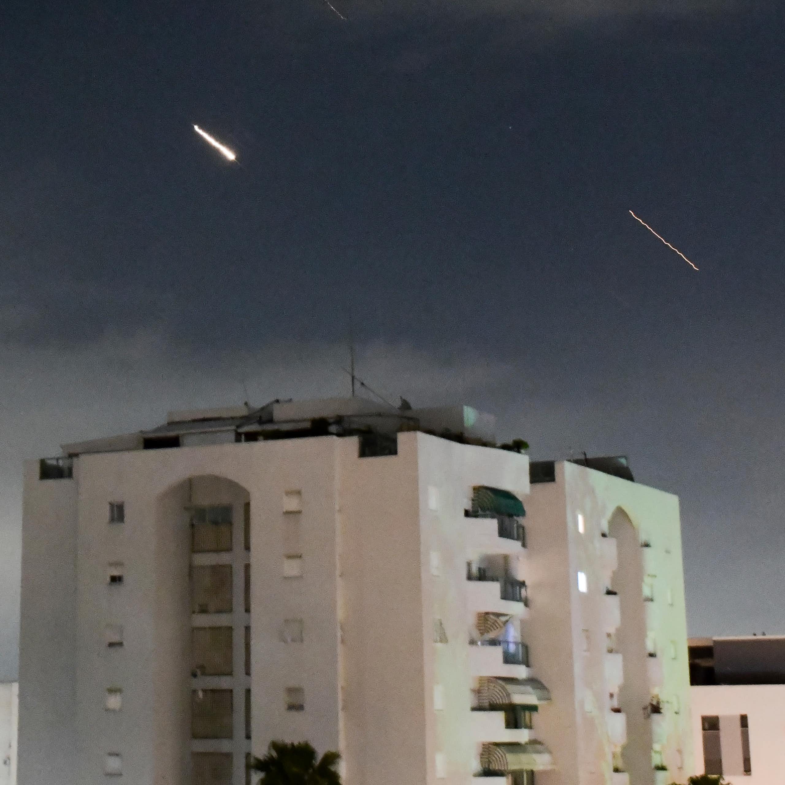 A white apartment building with streaks of light in the sky above it.