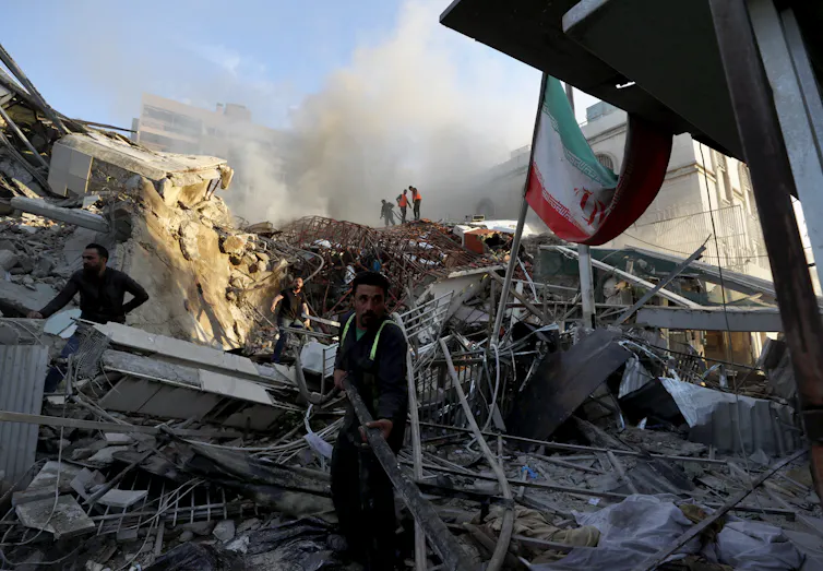 Emergency workers on a pile of smoky rubble.