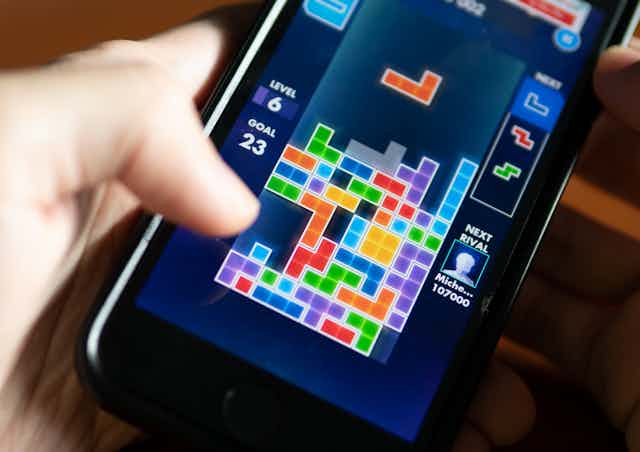 A person holding a smartphone displaying a tetris game.