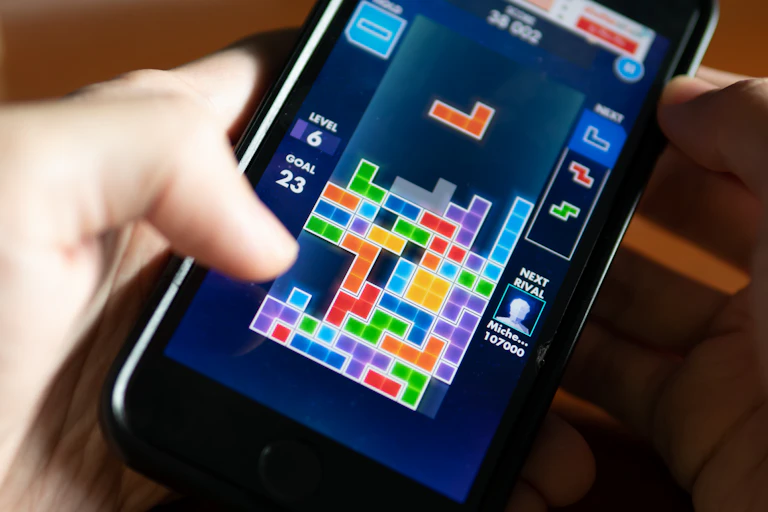A person holding a smartphone displaying a tetris game.