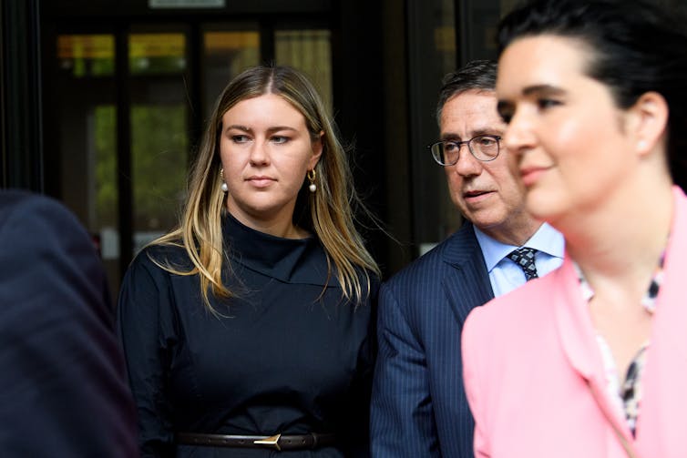 A woman in black walks out of a courtroom next to a man in a suit.