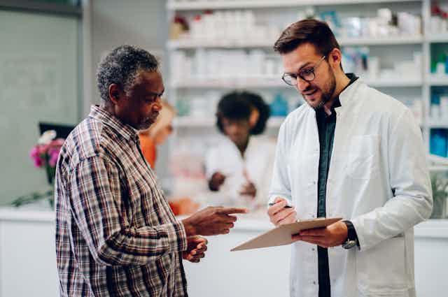 A pharmacist talking to a customer, showing him a clipboard.