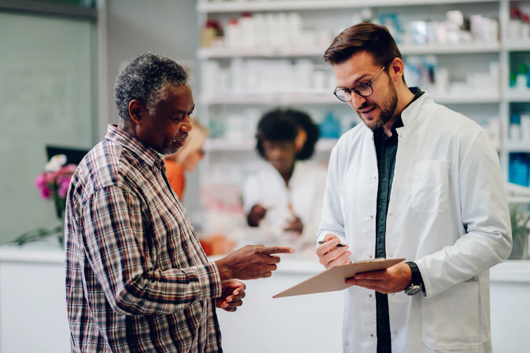 A pharmacist talking to a customer, showing him a clipboard.