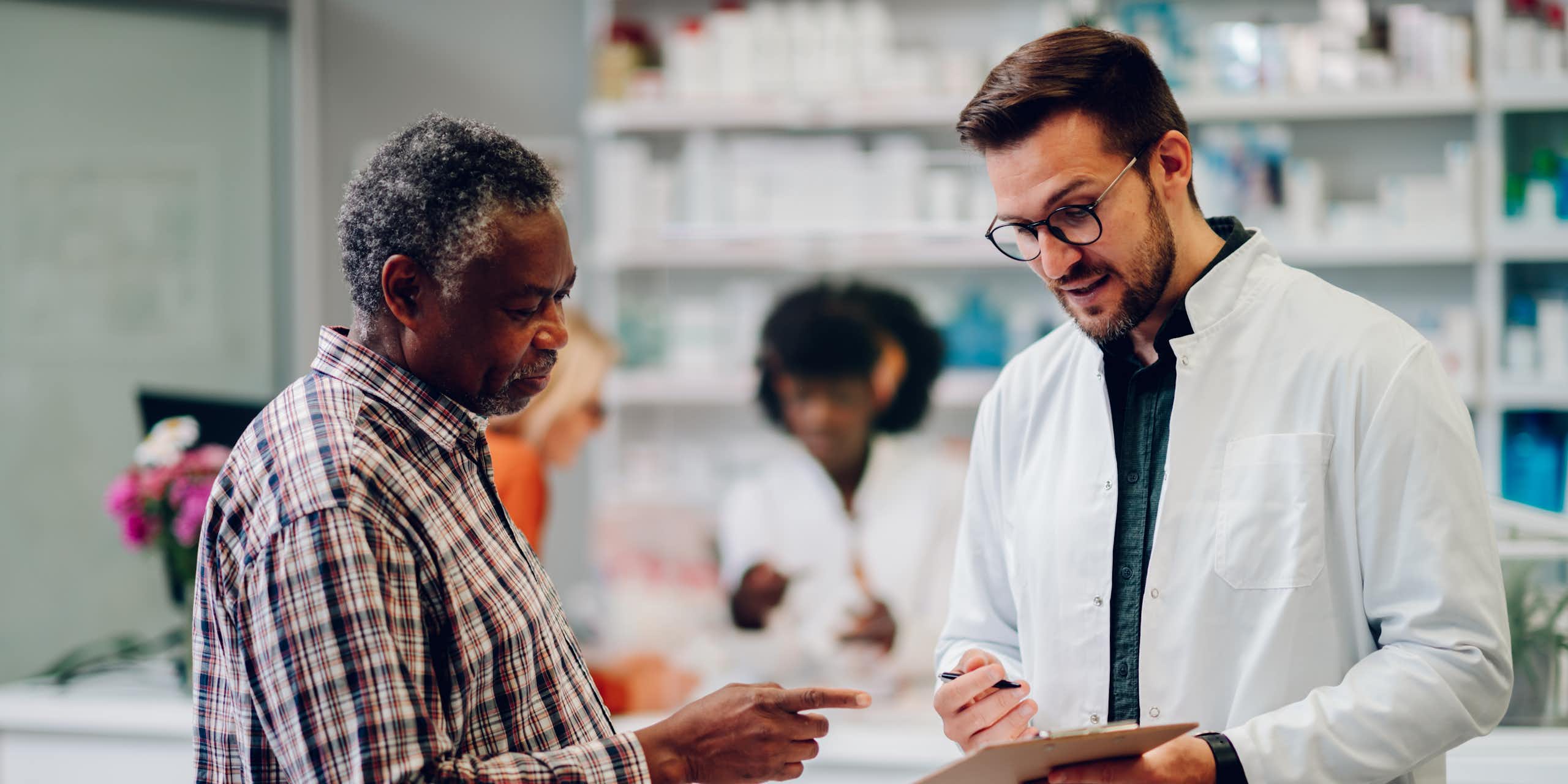 A pharmacist talking to a customer, showing him a clipboard.