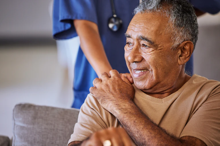 man sits with health worker behind him with their hand on his shoulder in supportive gesture