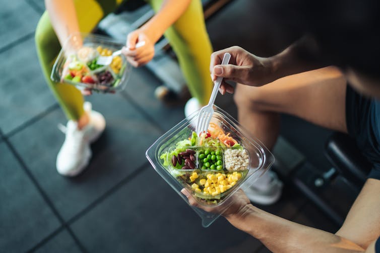 Two people sit down at the gym and eat a high-protein lunch.