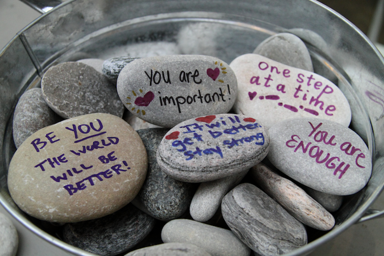 A bucket of rocks inscribed with inspirational messages such as 'You are enough' and 'One step at a time'