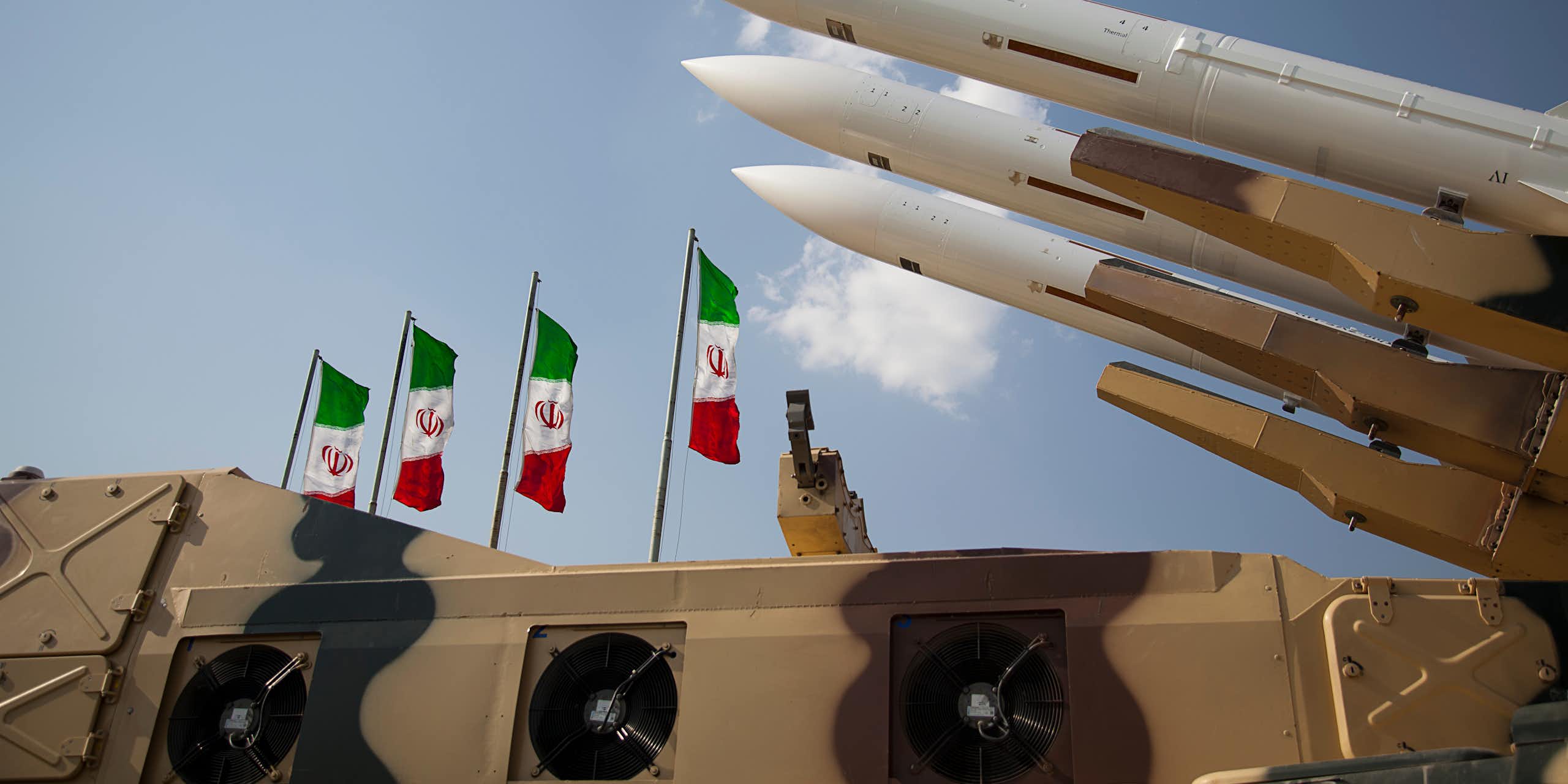 Three missiles pointing at the sky in front of four Iranian flags.