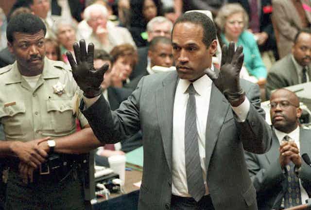 Un homme noir porte des gants noirs et lève les mains.