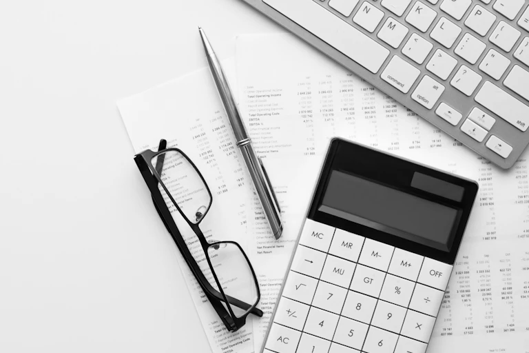 Imagen de una hoja de balances, unas gafas, un bológrafo, un teclado de ordenador y una calculadora.