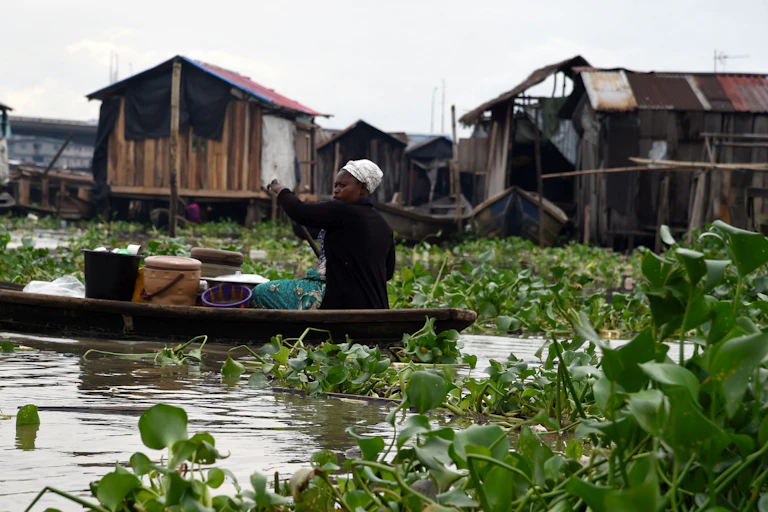 A woman vendor paddles her small boat through water in the Makoko waterfront settlement in Lagos, Nigeria