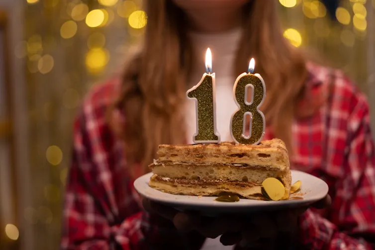 Une jeune femme portant un gâteau d’anniversaire avec des bougies indiquant 18 ans