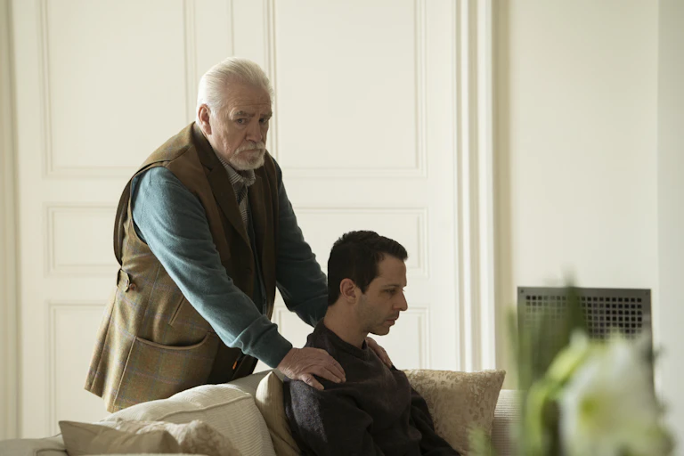 In a still from the HBO Series "Succession," patriarch Logan Roy, played by Brian Cox, is seen rubbing the shoulders of his son and heir apparent. Despite the seemingly affectionate gesture, the elder Roy looks off into the distance with a look of concern.