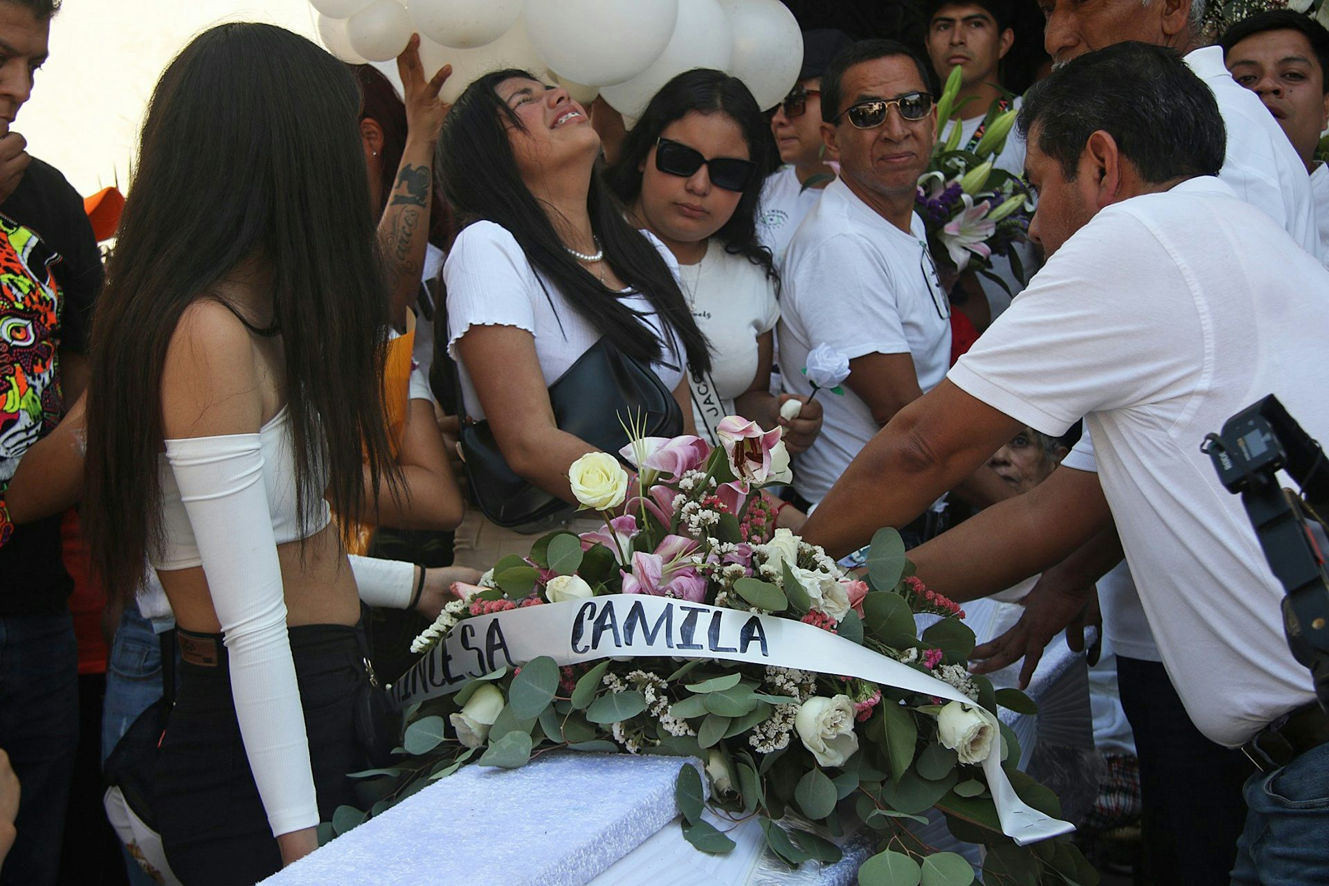 A group of people dressed in white standing around a coffin covered in flowers.